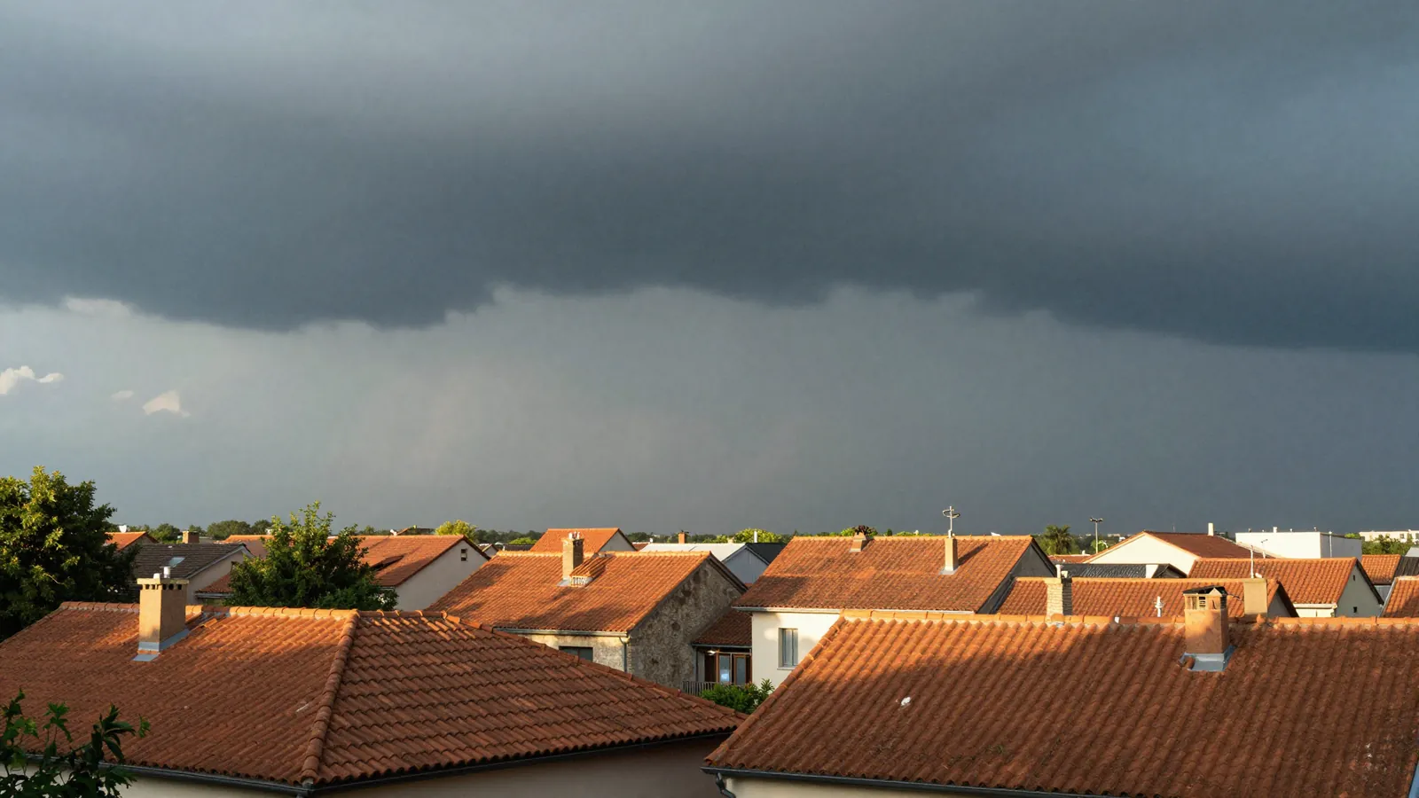 Ciel d'orage menaçant au-dessus d'un quartier résidentiel français à la fin d'une journée de canicule, premières gouttes de pluie